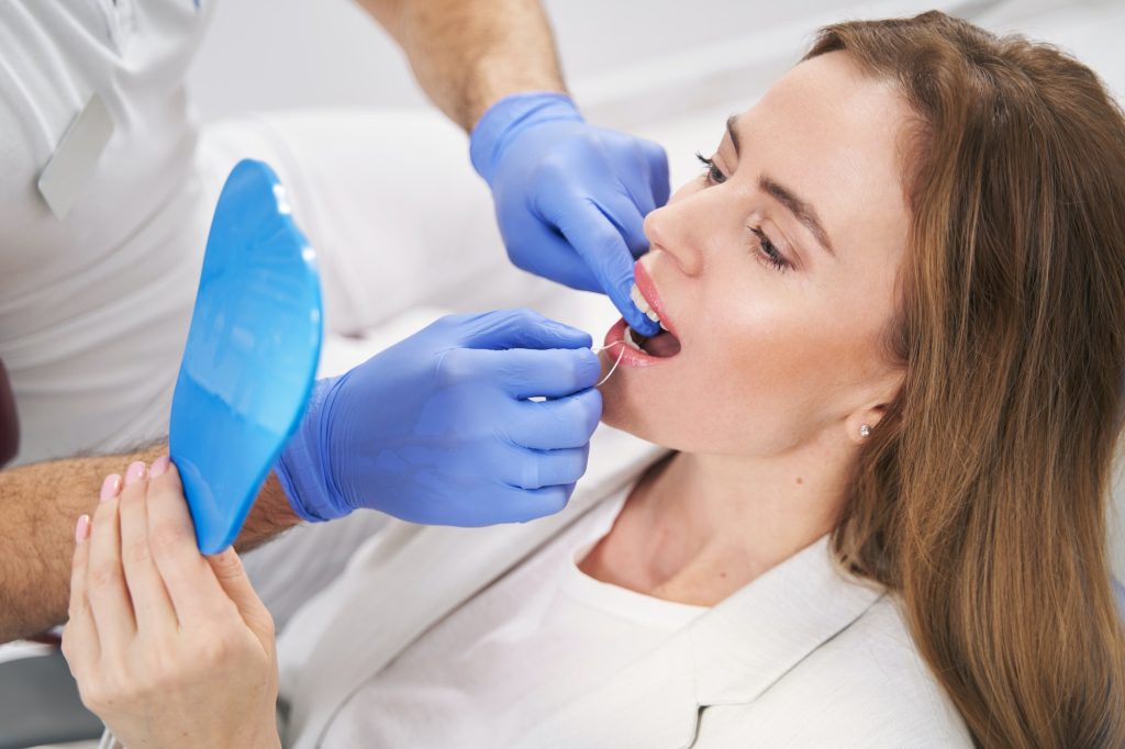 Dentist cleaning woman teeth with dental floss in clinic