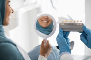 Restorative Dentistry. Muslim Female Patient Holding Mirror And Looking At Her Smile